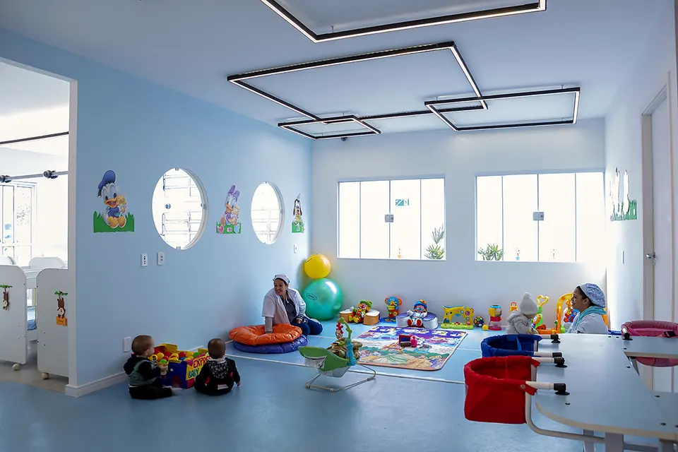 Sala de estimulação com crianças brincando no tapete e paredes com desenhos